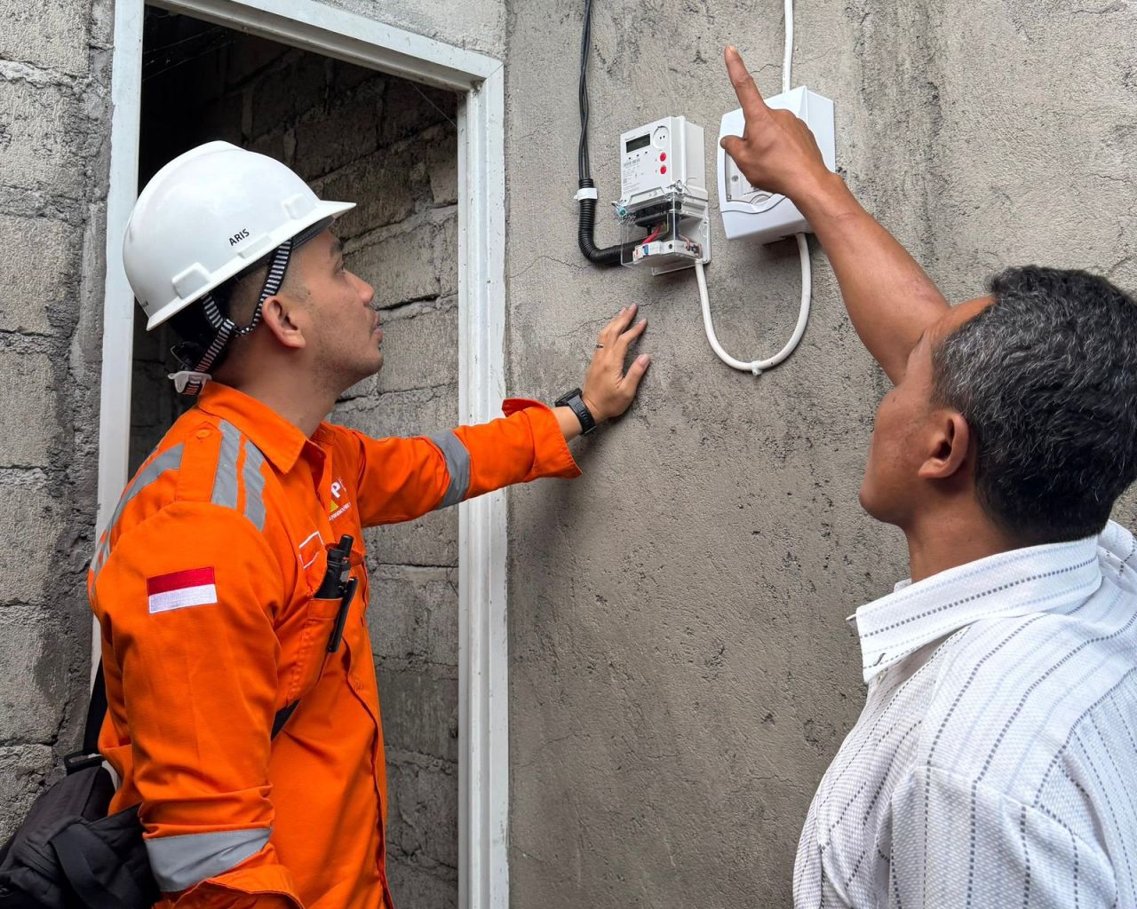 Salah satu penerima manfaat penyambungan listrik gratis program LUTD di Karangasem, Bali, I Wayan Polos (kanan) mendampingi petugas PLN saat menyalakan listrik di rumahnya untuk pertama kalinya.